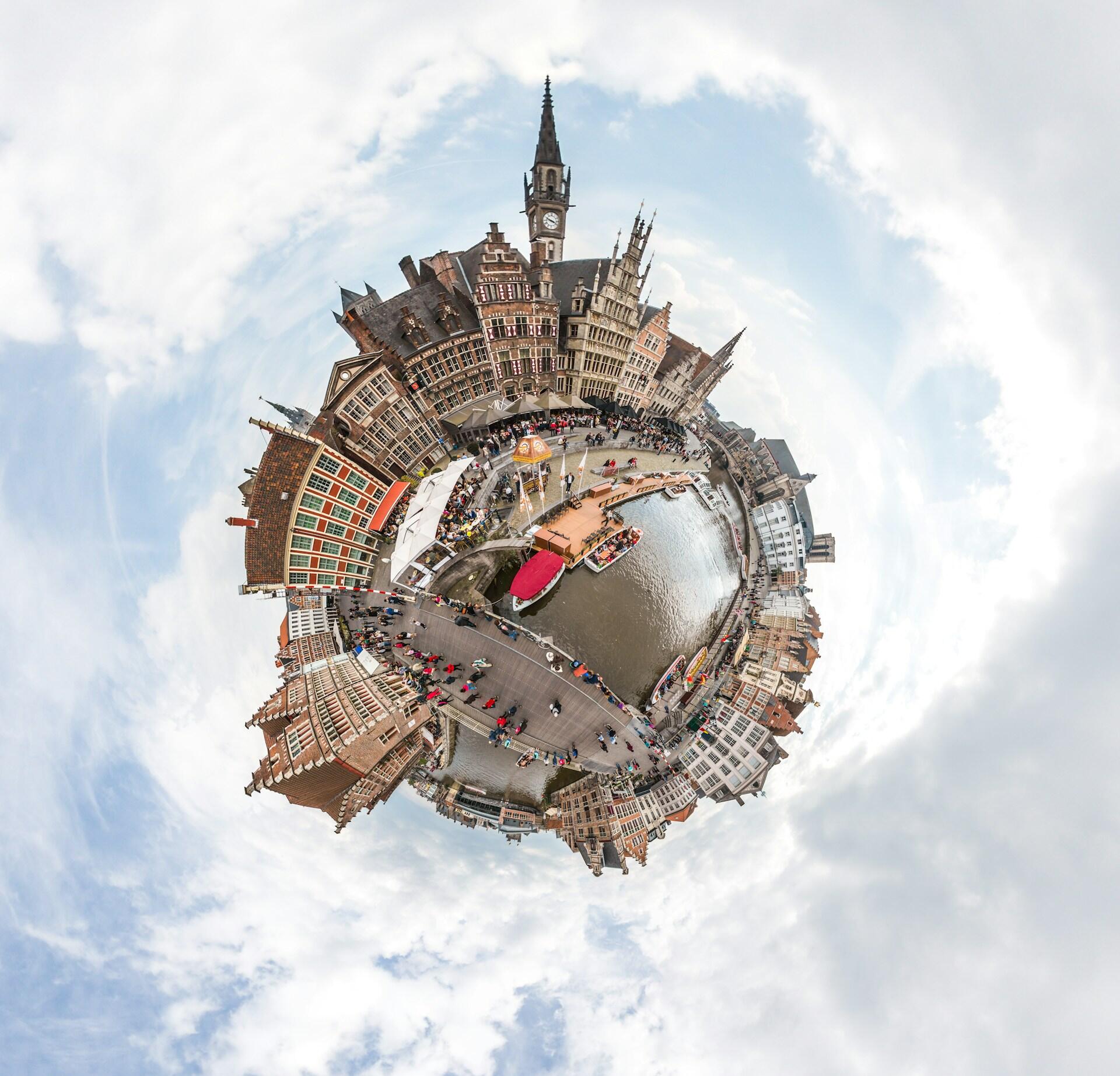 Miniaturwelt-Ansicht (Tilt-Shift) einer historischen europ&auml;ischen Stadt an einem Kanal, mit alten Geb&auml;uden, einem Uhrturm, Booten und vielen Menschen unter bew&ouml;lktem Himmel.